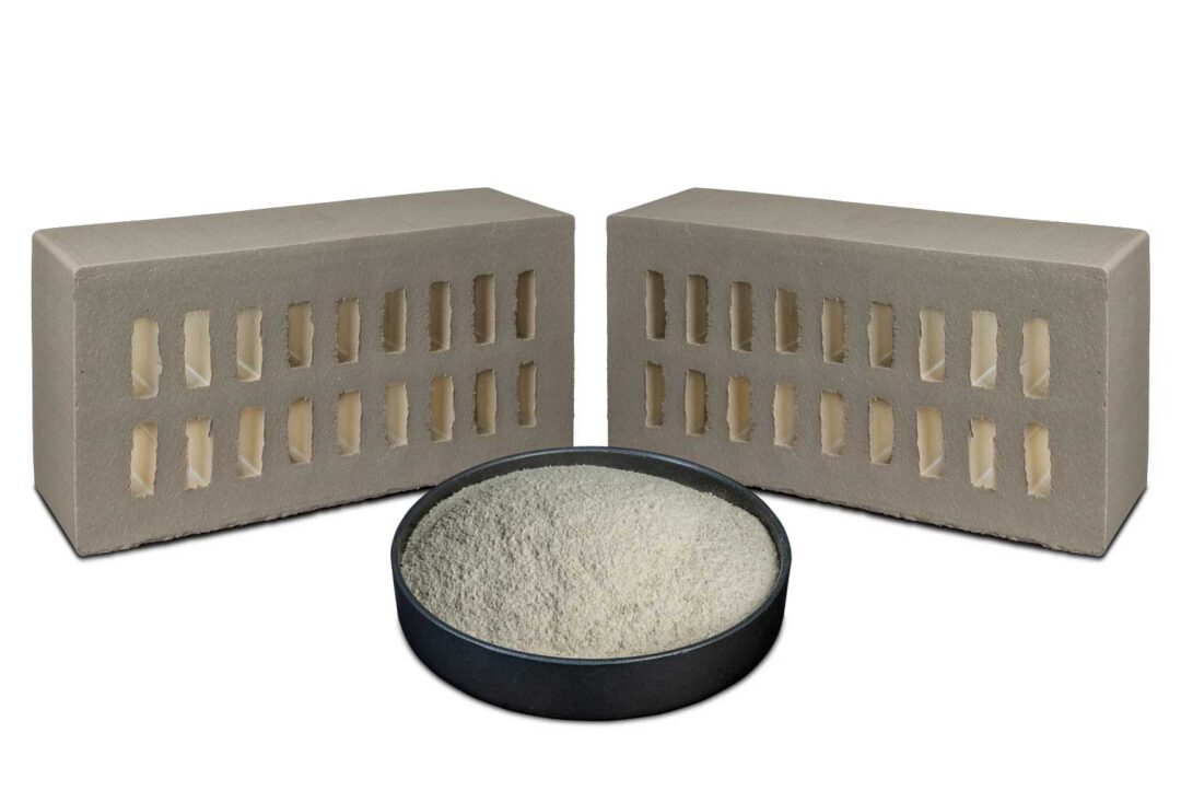 Weiße Mahlschamotte in einer dunklen Schale, dahinter zwei weiße Ziegelsteine.