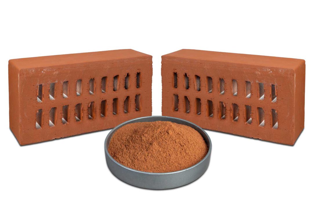 Rote Mahlschamotte in einer dunklen Schale, dahinter zwei rote Ziegelsteine.